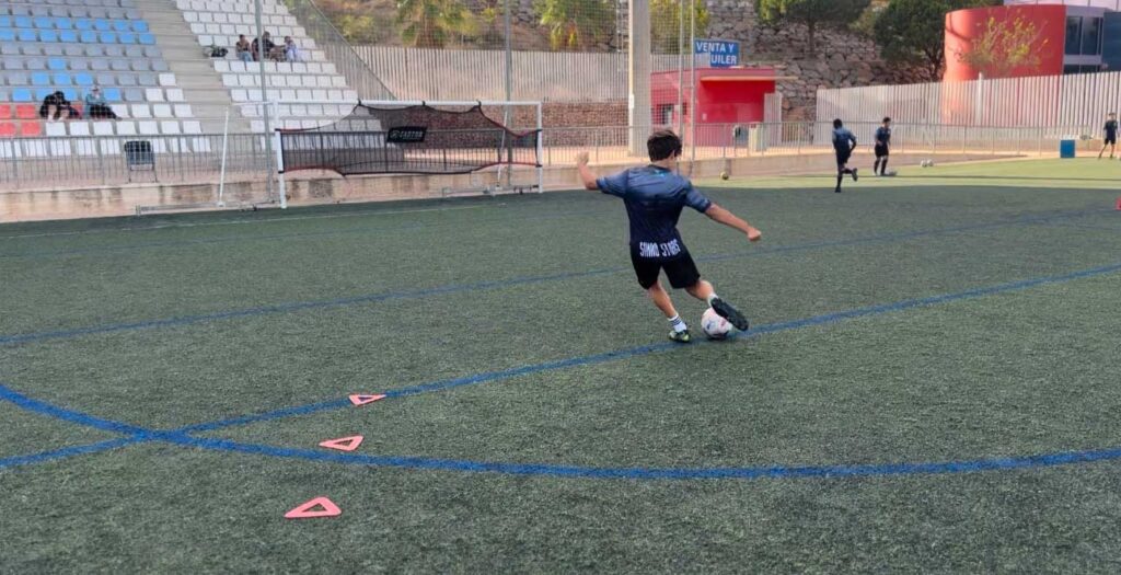 Un jugador de fútbol chutando un balón en un campo de césped artificial en la academia Simao Stars 20